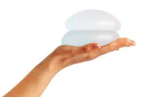 Hand holding two breast implants in relation to the dual plane breast augmentation procedure