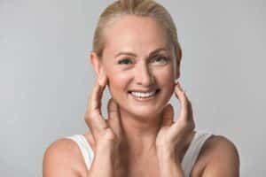 Smiling woman showcasing smooth skin and lifted jawline after dermal filler treatment for sagging jowls.