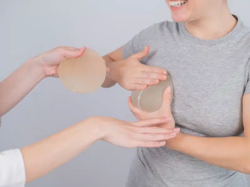 Woman holding breast implant while discussing replacement options with a medical professional.