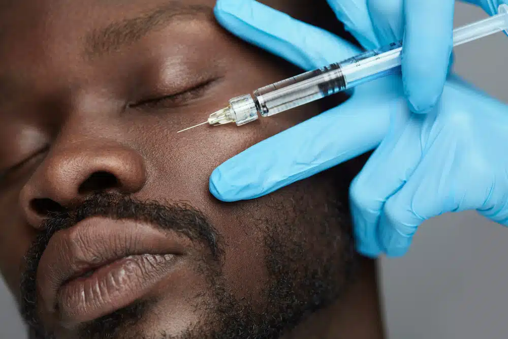 Close-up of man receiving dermal filler injection near eye area for facial contouring and skin refinement.
