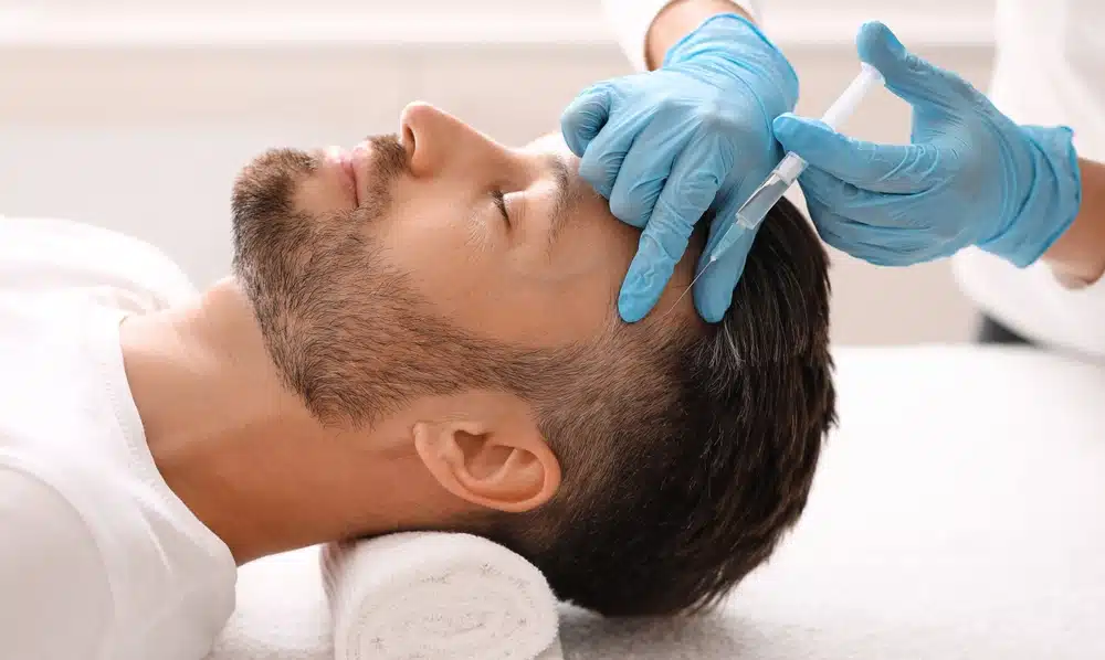 Man lying down receiving Botox injection in forehead to reduce wrinkles while maintaining natural expression.