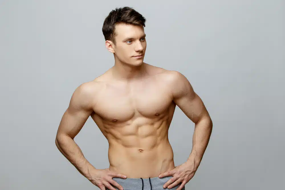 Fit man with sculpted chest and abs, showing defined results from male breast reduction and pec enhancement.