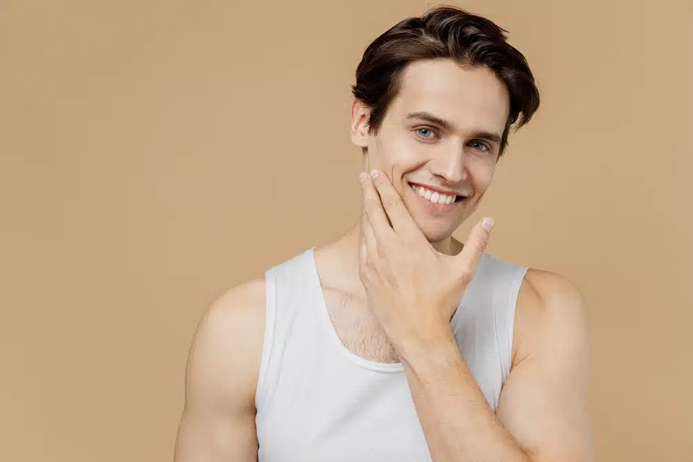 Smiling man with clear skin in white tank top showing confident results from male cosmetic procedure.