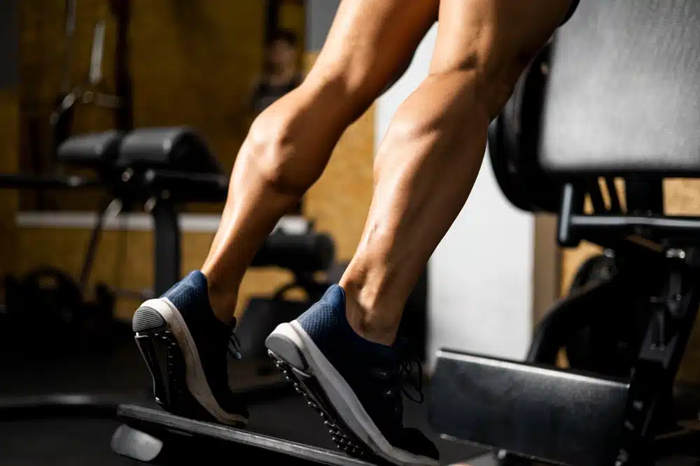 Close-up of lower legs performing calf raises in gym, highlighting muscle definition and calf implant potential