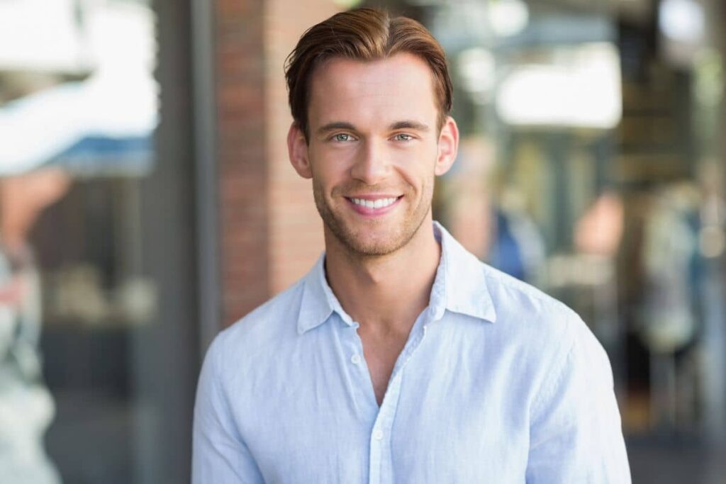 Smiling man in light blue shirt with smooth skin and defined features after non-surgical facial enhancement treatments