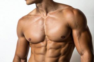 A close-up of a muscular man's torso and chest, highlighting well-defined pectoral and abdominal muscles achieved through bodybuilding and athletic training.