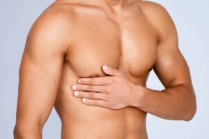 A close-up of a shirtless man resting his hand over his pectoral muscle to illustrate the area of focus for post-operative care and recovery.