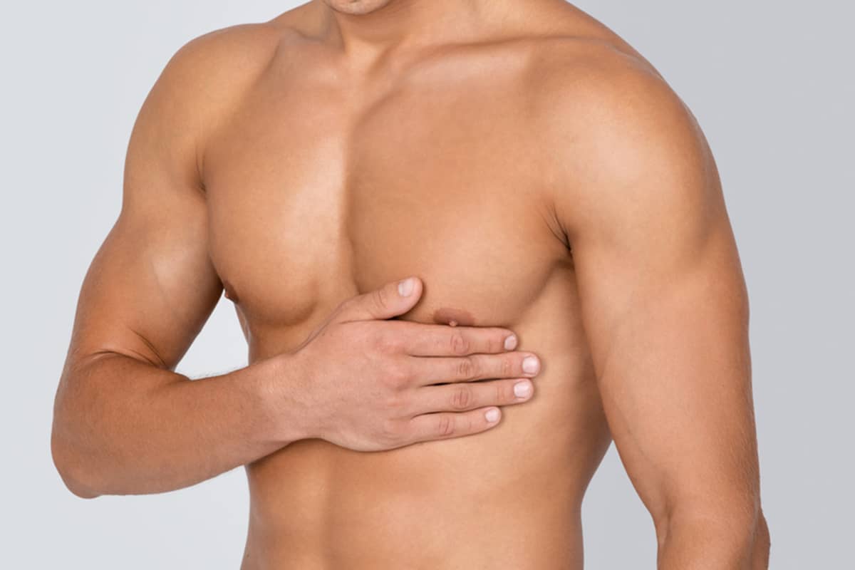 A close-up of a fit man’s torso with his hand resting on his pectoral muscle, showcasing the natural contours of the male chest.