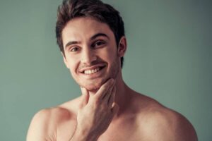 A smiling man touching his chin to highlight a well-defined and projected chin structure.